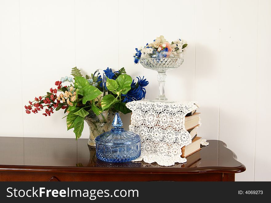 Stylish home decor arrangement with flowers, crystal, china, books, and an antique doily.