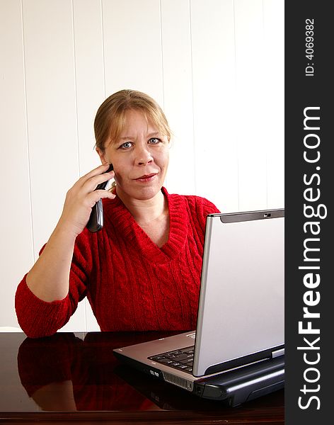 Woman in red sweater working at a laptop computer while talking on cell phone. Woman in red sweater working at a laptop computer while talking on cell phone