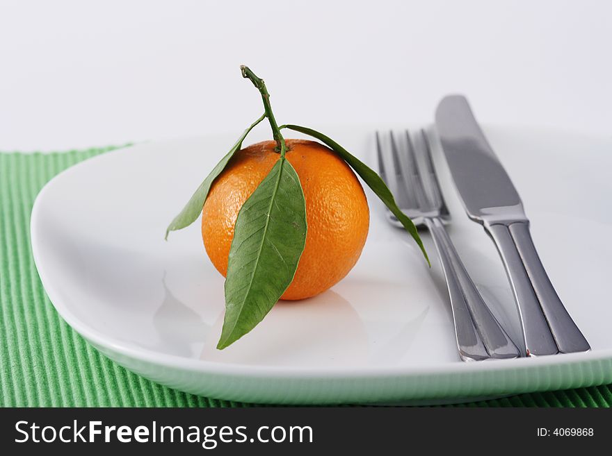 Mandarine with leaves on a white plate with knife and fork. Mandarine with leaves on a white plate with knife and fork