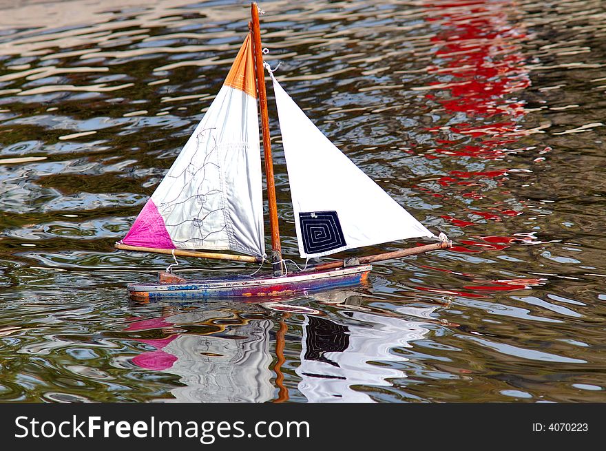 France, Paris:water reflects and  Little toy boat with white sails. France, Paris:water reflects and  Little toy boat with white sails