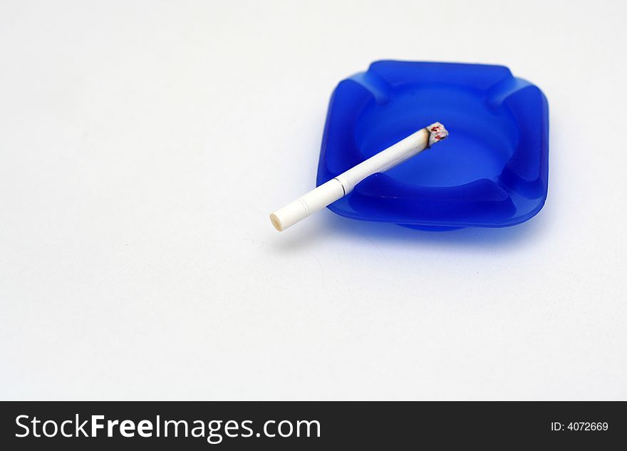 White cigarette on blue ashtray with white background. White cigarette on blue ashtray with white background