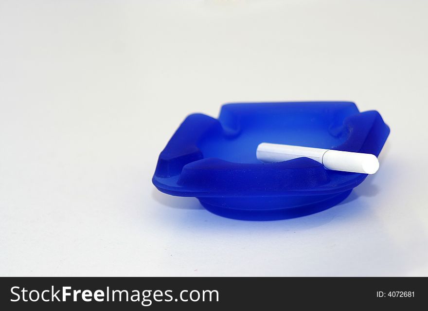 White cigarette on blue ashtray with white background. White cigarette on blue ashtray with white background