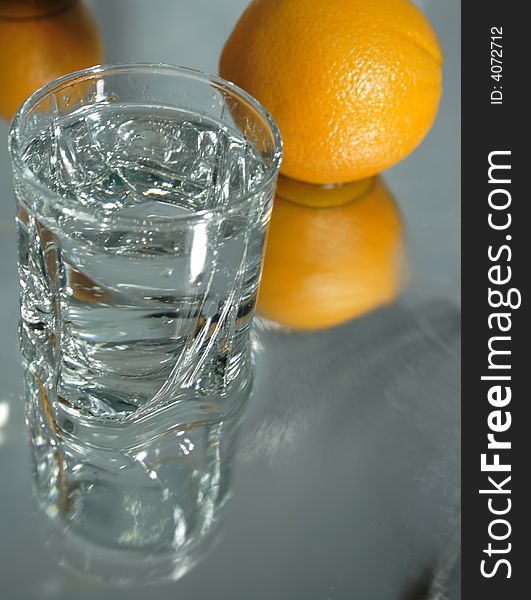 Glass of clear water with ice on background with two oganges. Glass of clear water with ice on background with two oganges