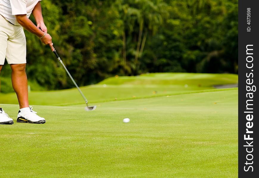 Golfer putting on green,with blurred moving club and ball