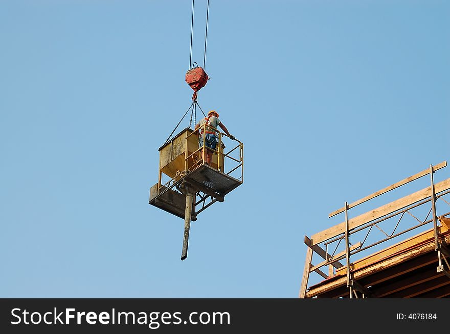 Construction worker being transported by jib crane with concrete mix charging hopper onto building platform. Construction worker being transported by jib crane with concrete mix charging hopper onto building platform