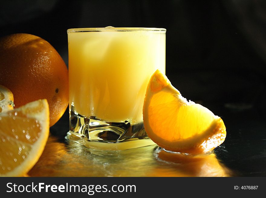 Slit orange and glass of orange juice with ice on dark. Slit orange and glass of orange juice with ice on dark
