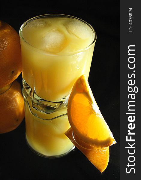 Slit orange and glass of orange juice with ice on dark. Slit orange and glass of orange juice with ice on dark