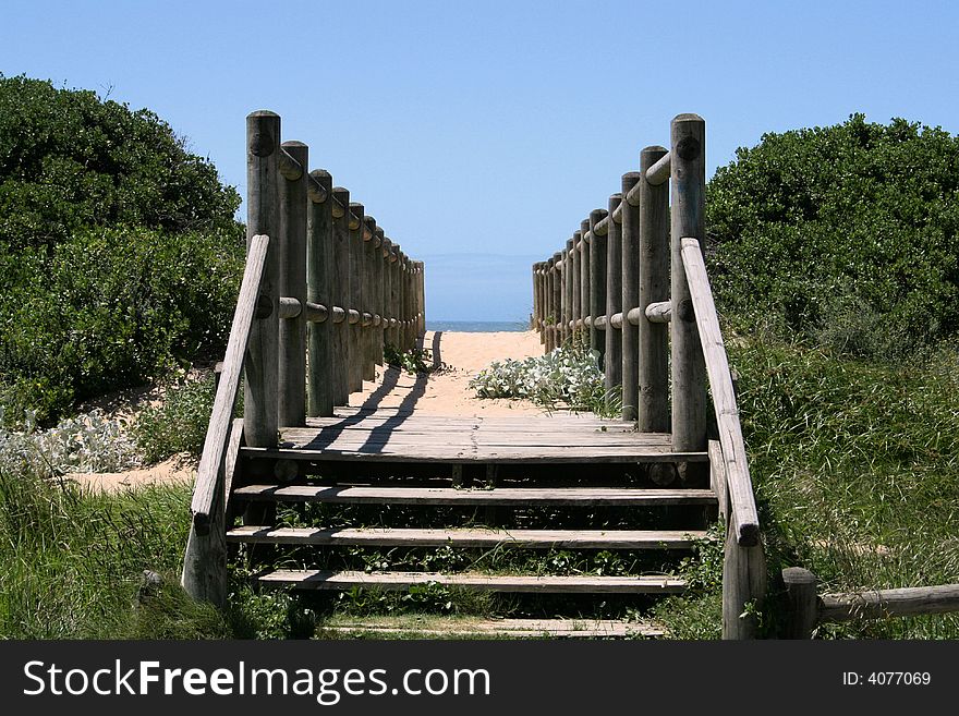 A wooden walkway or bridge going over a sand dune to the beach with the sea and sky in the background. A wooden walkway or bridge going over a sand dune to the beach with the sea and sky in the background