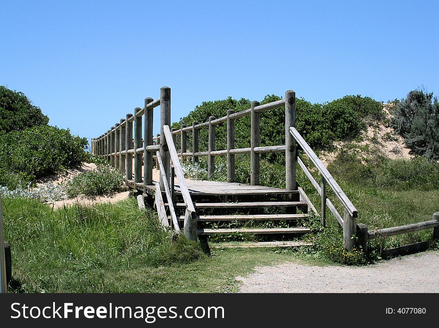 A wooden walkway or bridge going over a sand dune to the beach with the sea and sky in the background. A wooden walkway or bridge going over a sand dune to the beach with the sea and sky in the background