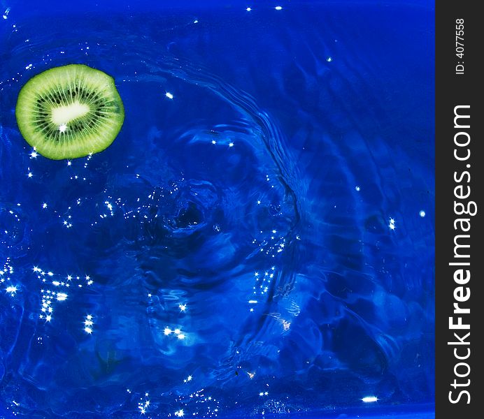 Slice of kiwi fruit fallen in water and waves on water from its falling. Slice of kiwi fruit fallen in water and waves on water from its falling
