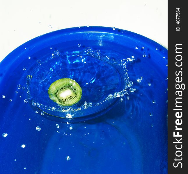 Slice of kiwi fruit fallen in water and a crown of water from its falling