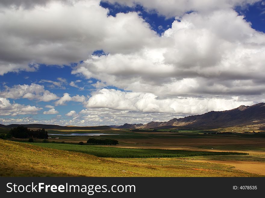 Landscape with blue sky, clouds, blue lake, green trees and grass, yellow sand and red ground, ridge of mountains in South Africa. Landscape with blue sky, clouds, blue lake, green trees and grass, yellow sand and red ground, ridge of mountains in South Africa