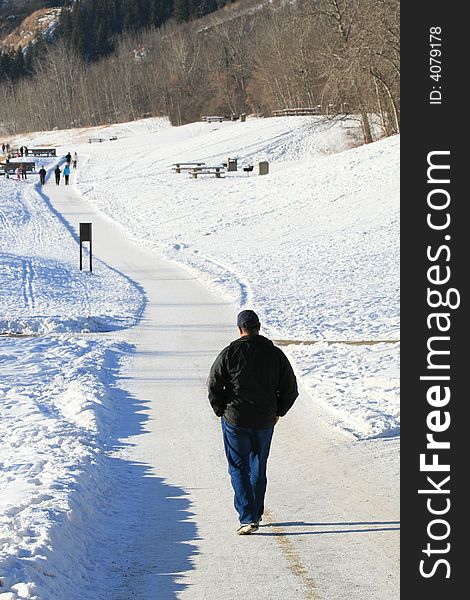 A man taking a stroll down a snowy path in a riverfront park in a city. A man taking a stroll down a snowy path in a riverfront park in a city