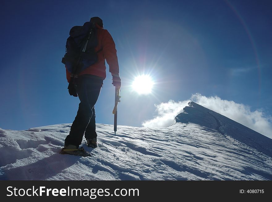 A lone climber reaching the summit of the mountain; back lite. West Alps, Swiss. A lone climber reaching the summit of the mountain; back lite. West Alps, Swiss.