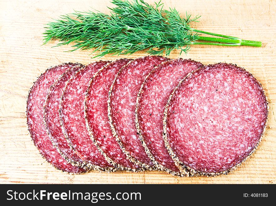 Peppered salami with dill on a wooden chopping block