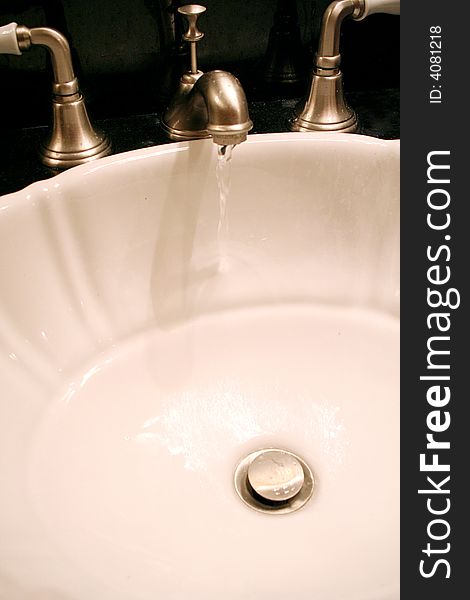 A faucet trickles water in a bathroom sink. A faucet trickles water in a bathroom sink.