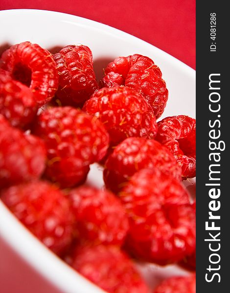 A dish of raspberries with a red background