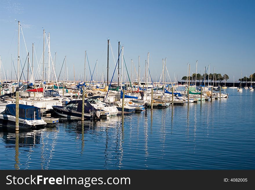 Sail boats moored diagonally in a marina, reflected in the blue water. Sail boats moored diagonally in a marina, reflected in the blue water