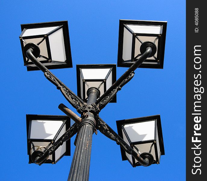 Three ornate street lamps on a lamp post against a blue sky in Romania