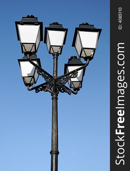 Three ornate street lamps on a lamp post against a blue sky in Romania