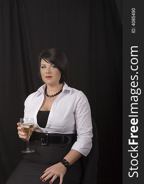 A model with black hair and white blouse sitting in a chair with a glass of wine on a black background. A model with black hair and white blouse sitting in a chair with a glass of wine on a black background