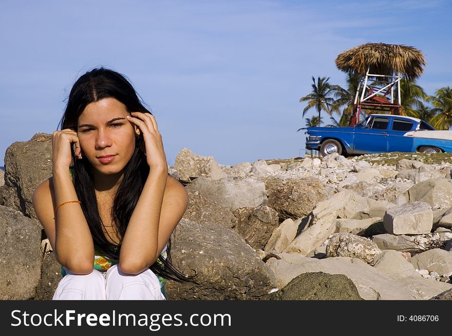 Beautiful girl sitting on rocky beach - vintage car on the background