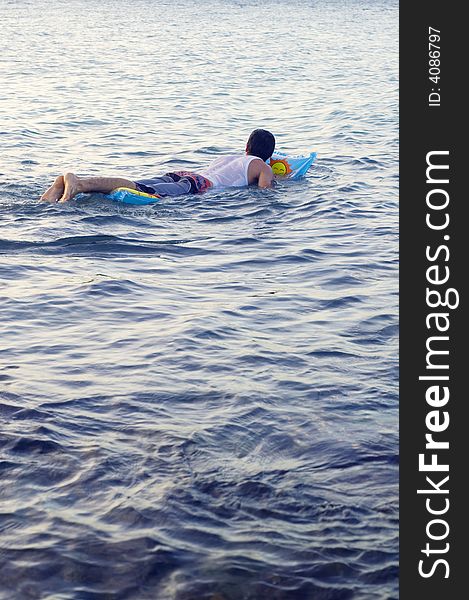 Boy swimming on a raft with ocean waves background