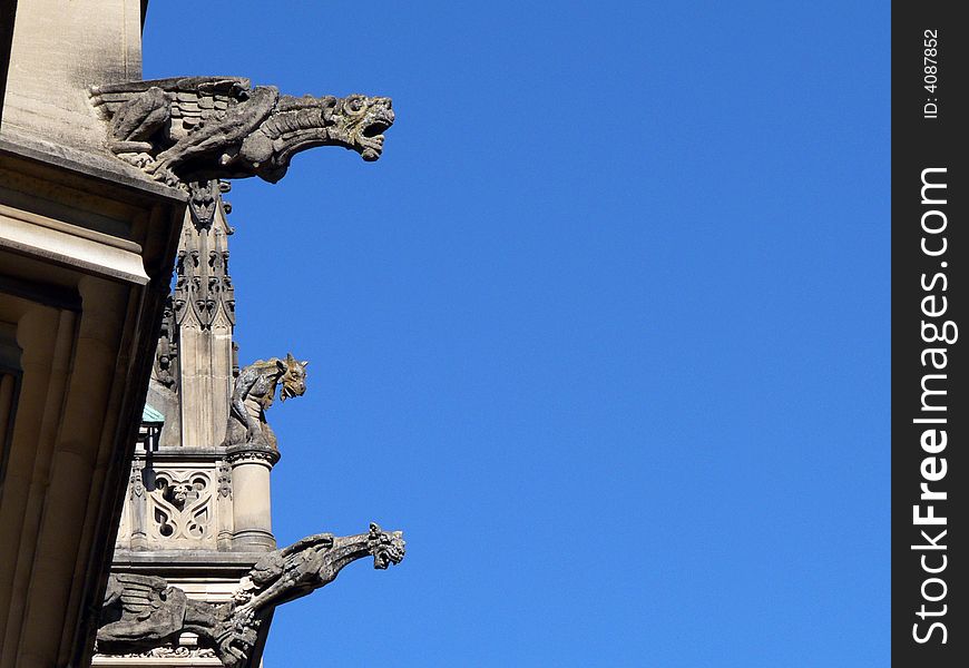 Three Gargoyles on the roof of a European style building menacingly look down from above.