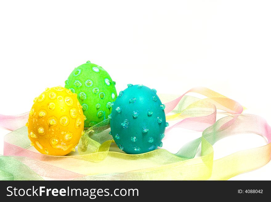 Three Easter eggs with speckles and glitter in a multicolored ribbon nest. Three Easter eggs with speckles and glitter in a multicolored ribbon nest.