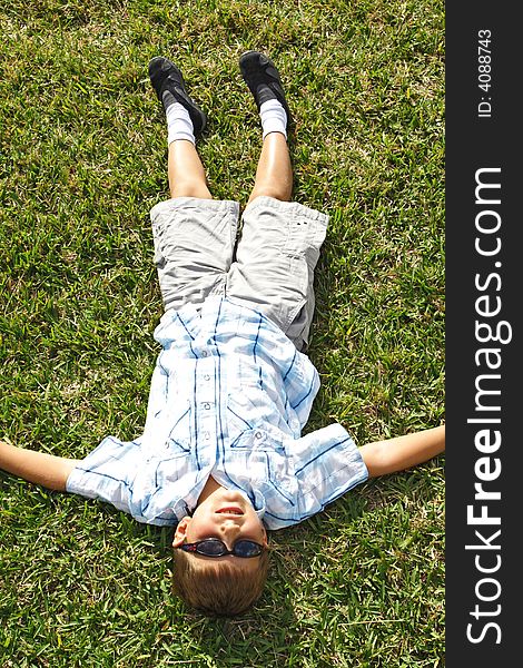 Little kid lying on the grass wearing sunglasses.