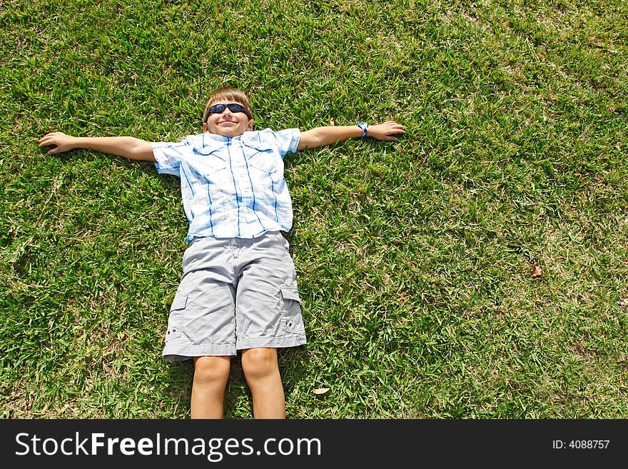Little kid lying on the grass wearing sunglasses.