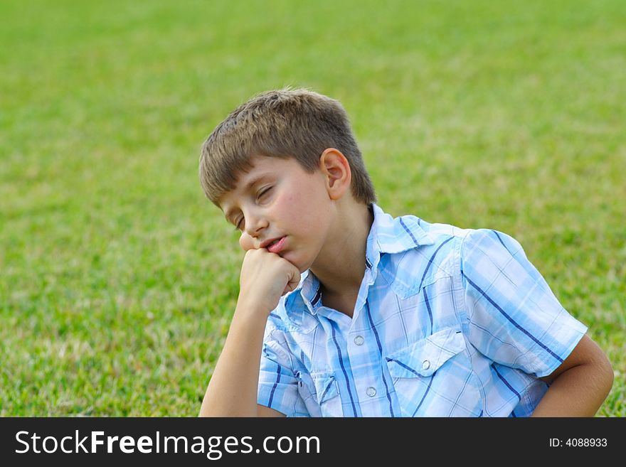 Boy day dreaming on a green field of grass