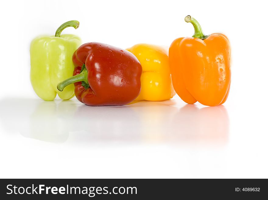 Four colored peppers isolated on white with reflection on glossy surface.