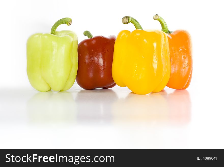 Four colored peppers isolated on white with reflection on glossy surface.