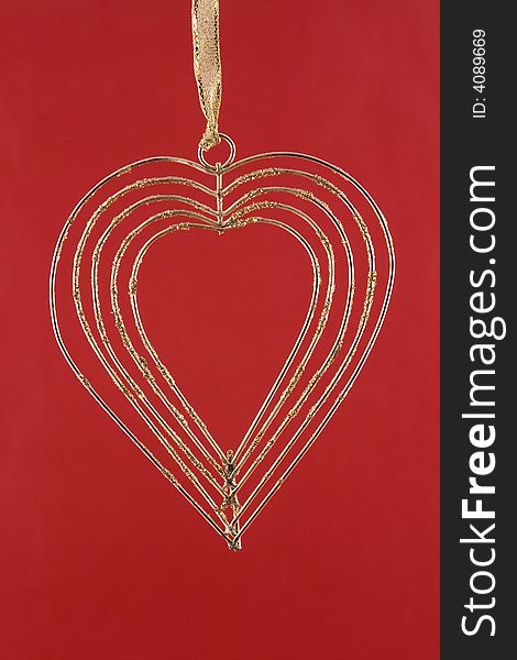 Gold heart from a wire on a gold tape isolated on a red background. Gold heart from a wire on a gold tape isolated on a red background