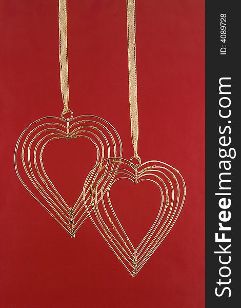 Two gold hearts from a wire on a gold tape on a red background. Two gold hearts from a wire on a gold tape on a red background