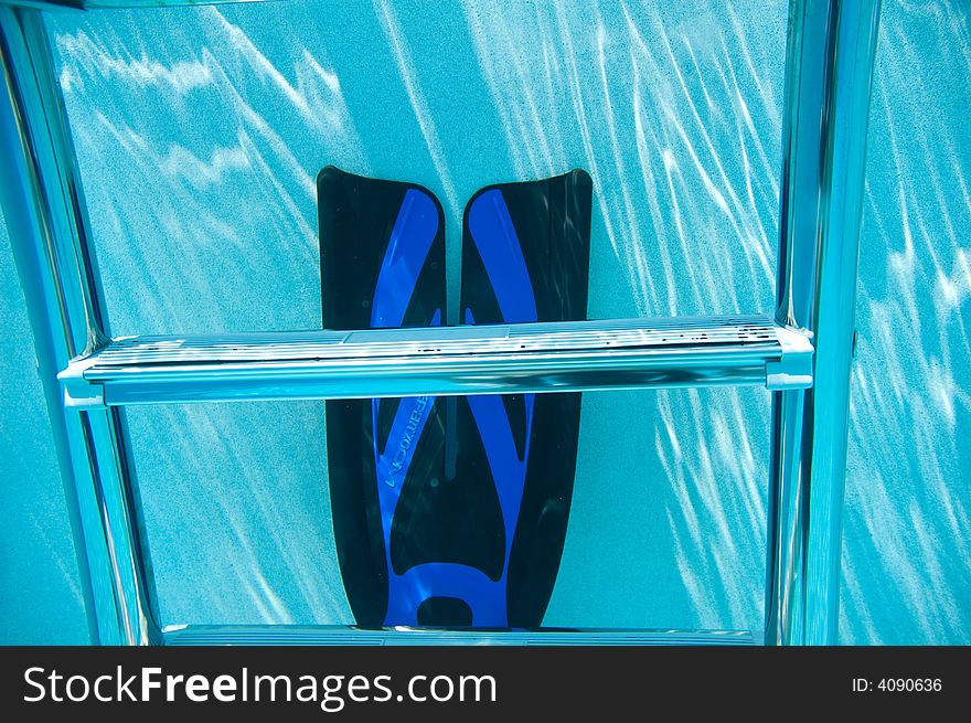 Horizontal view of underwater pool ladder and one swim fin in clear blue water. Horizontal view of underwater pool ladder and one swim fin in clear blue water
