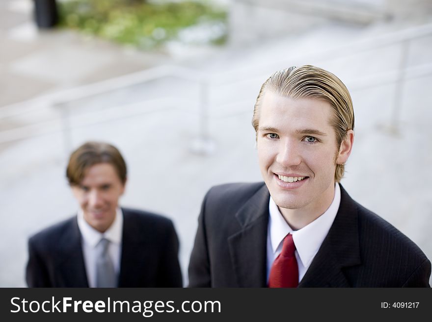 Two businessmen standing next to each other looking up at camera, smiling. Two businessmen standing next to each other looking up at camera, smiling