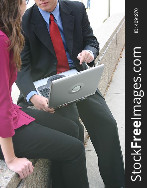 Businessman and businesswoman sit outside face each other with laptop between them. Businessman and businesswoman sit outside face each other with laptop between them