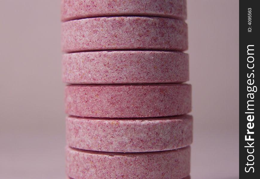 Stack of pink and purple multivitamins, isolated on dark pink background, closeup macro. Stack of pink and purple multivitamins, isolated on dark pink background, closeup macro