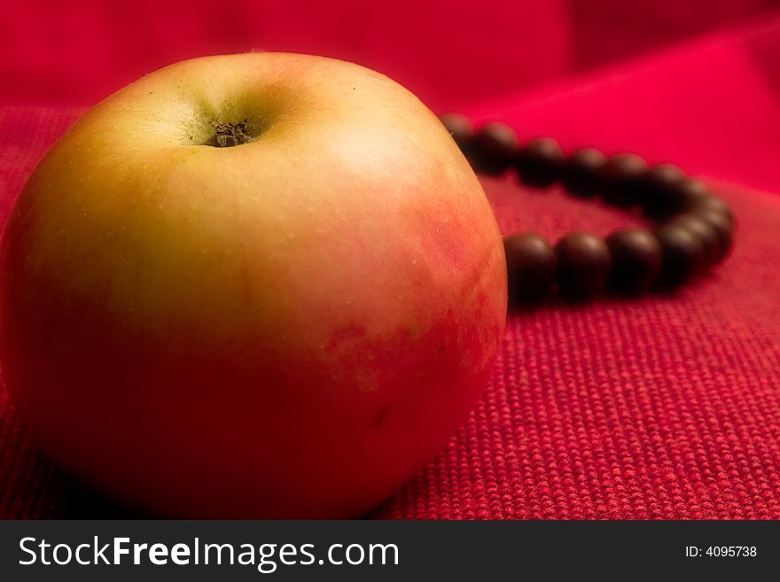 Single apple red background close up macro prayer beads behind. Single apple red background close up macro prayer beads behind