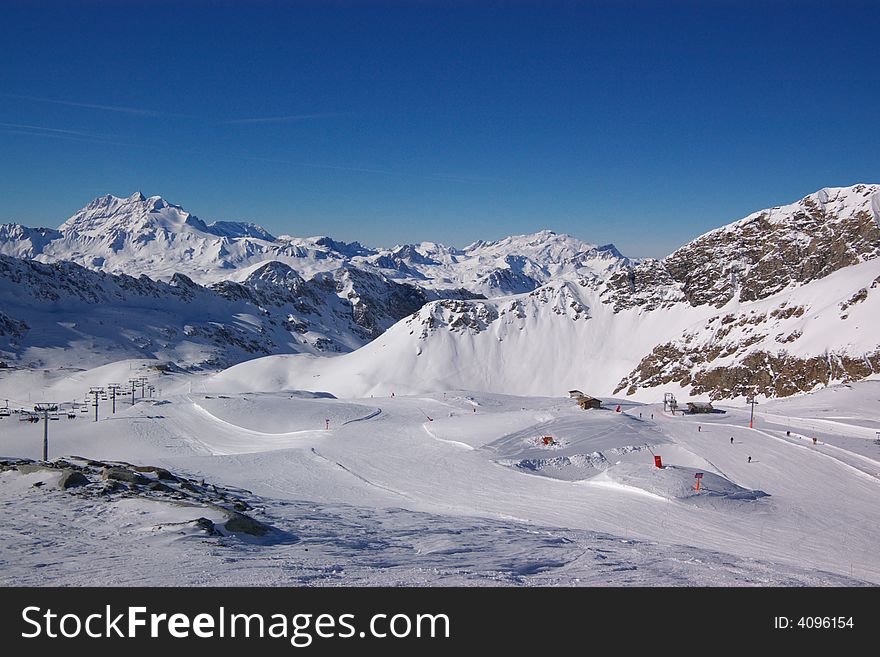 View on alpine snow winter mountains chain and ski bench lift under blue sky. Alps, France, Europe. View on alpine snow winter mountains chain and ski bench lift under blue sky. Alps, France, Europe.