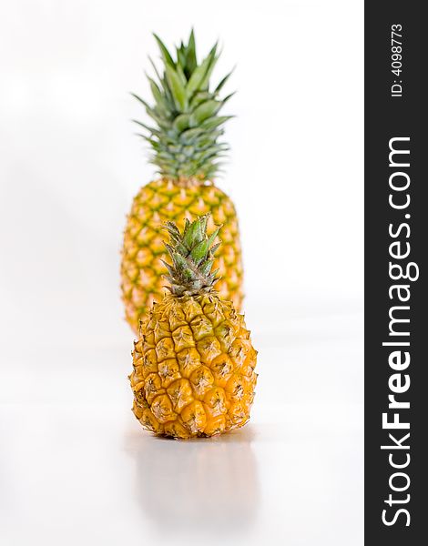 Isolated baby and normal pineapple fruits reflecting on white glossy surface. Isolated baby and normal pineapple fruits reflecting on white glossy surface.