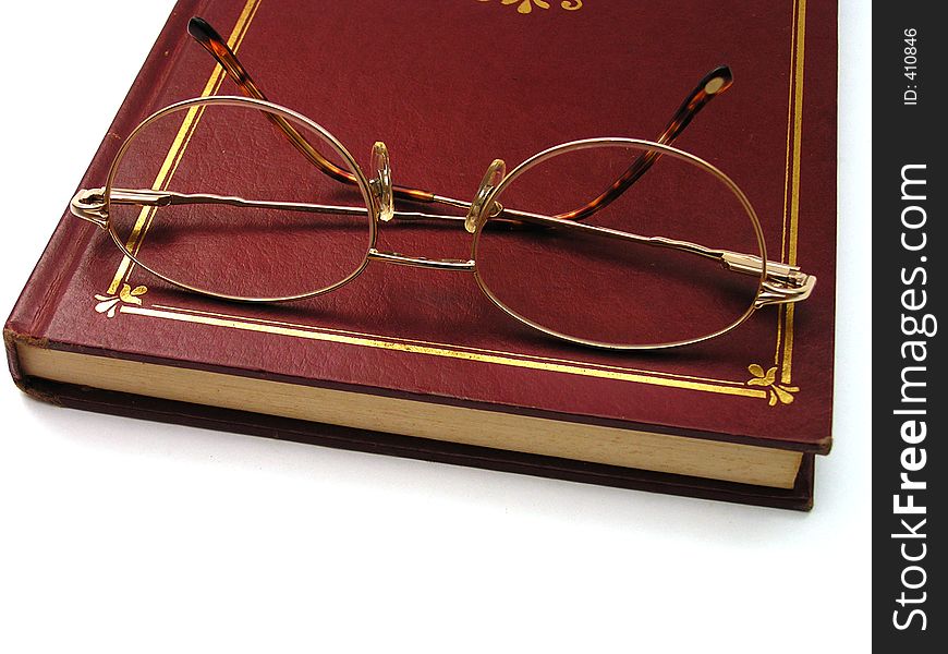 Reading glass on top of a dark red hardcover book, focus on the centre of the eyeglass.