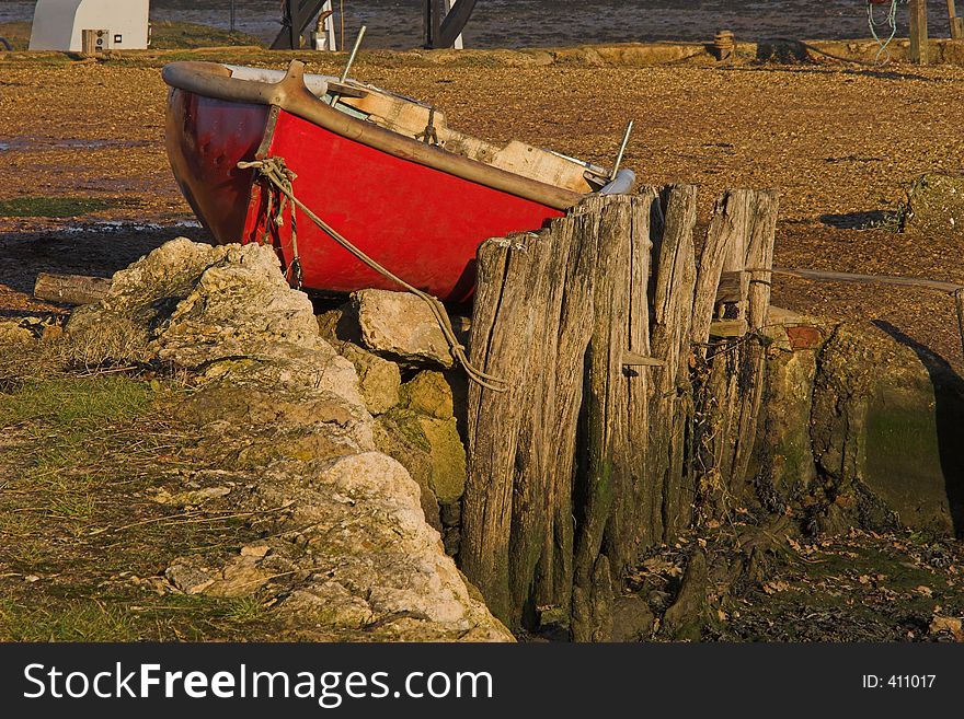 Red small rowing boat berthed on land with wooden stay. Red small rowing boat berthed on land with wooden stay.