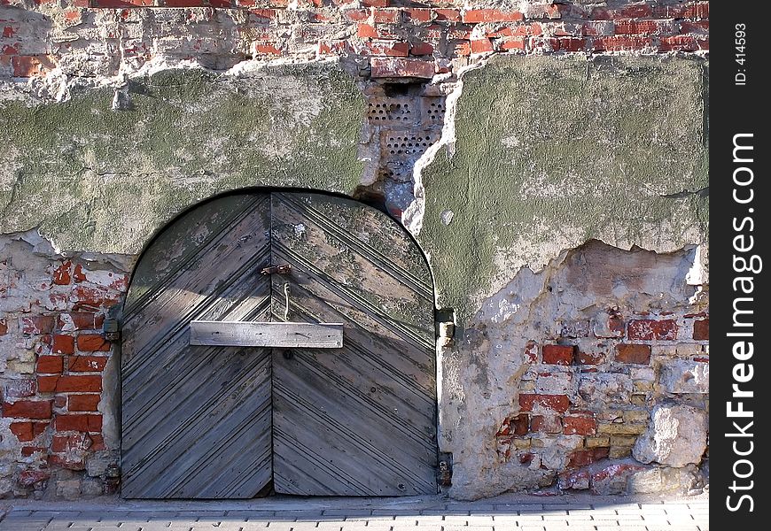 Old wooden door on a background of the destroyed stone wall. Old wooden door on a background of the destroyed stone wall.