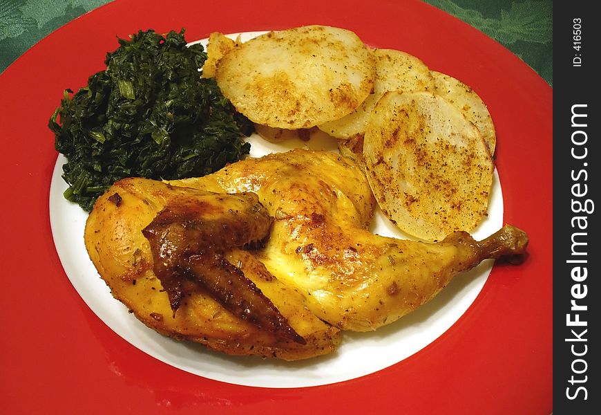 Photo of cornish game hen, potatos and spinach served on a red Christmas plate.