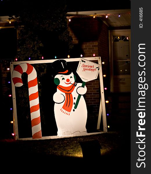 A snowman and candy cane decorate the front lawn of a home during the holiday season.