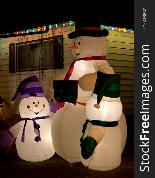 Thre snowmen decorate the front lawn of a home during the holiday season. Thre snowmen decorate the front lawn of a home during the holiday season.
