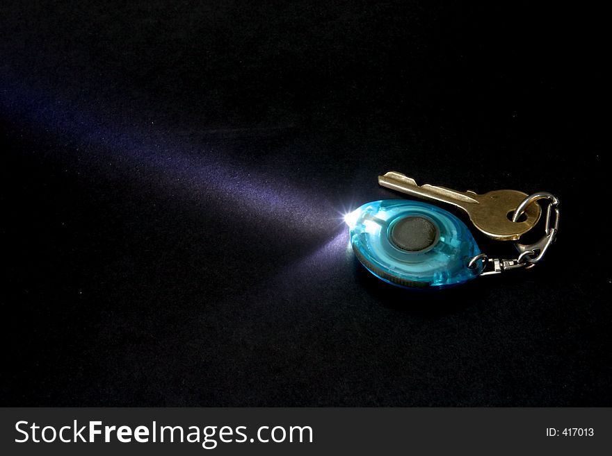 Key ring flashlight with door key - isolated on black. Key ring flashlight with door key - isolated on black